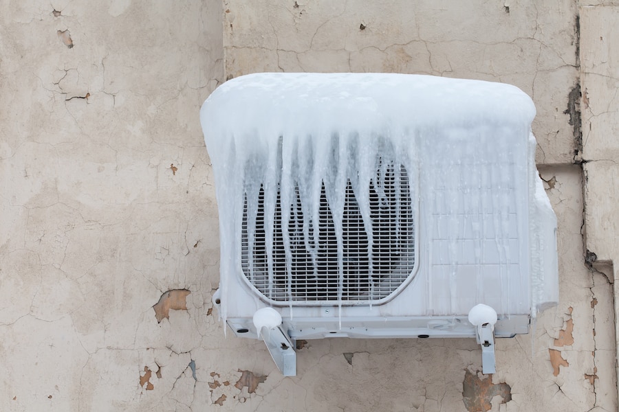 Air conditioner with frozen ice and icicles. Cooling, cold temperature concept image. Aged wall background.