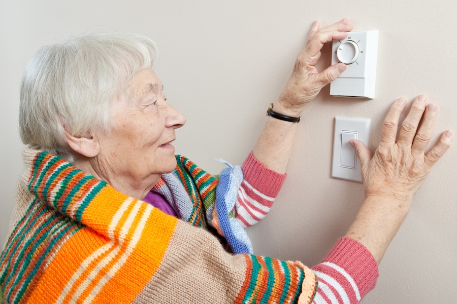 Senior woman saving energy by dressing warm and adjusting her thermostat.