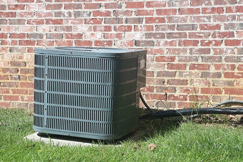 Home Air Conditioner Condenser coil sitting in front of brick wall